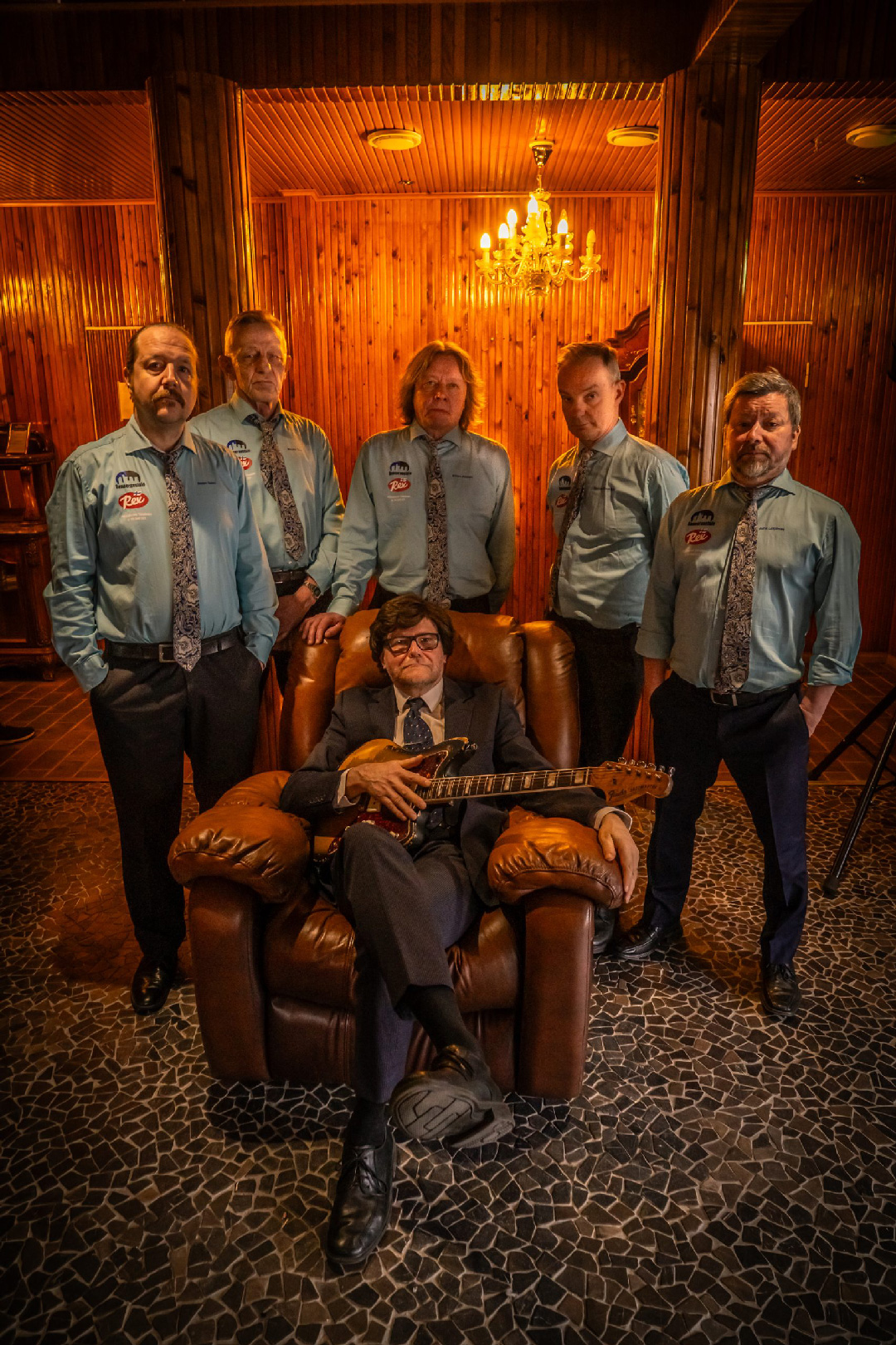 Martti Servo istuu nojatuolissa keskellä, bändi seisoo takana
